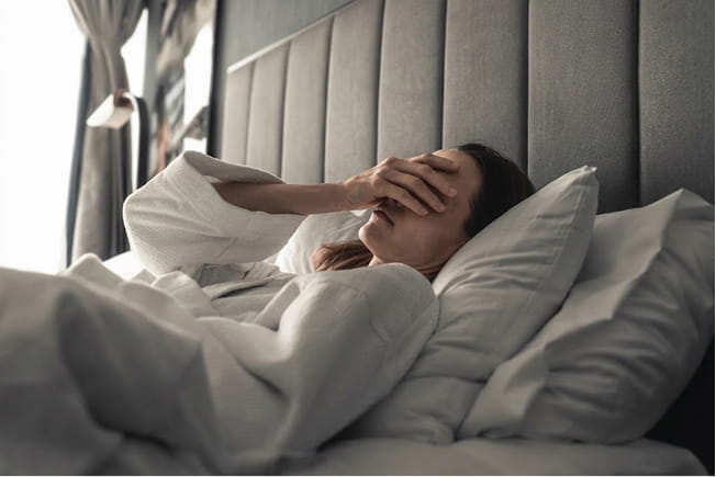 Cama deshecha a la mañana con una taza en la mesa de luz
